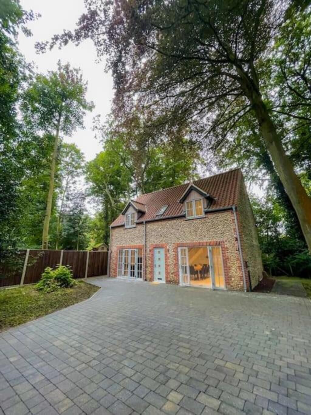 Une maison à deux étages, avec une façade en briques, un toit en tuiles et une allée pavée menant à un portail en bois.