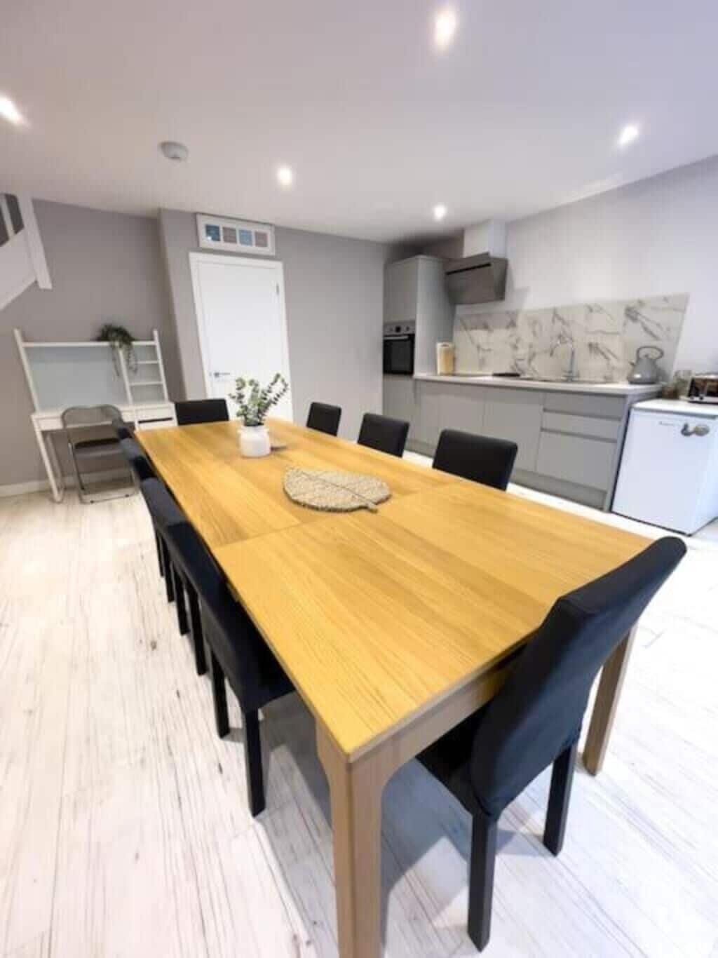 A modern dining area with a wooden table and black chairs, a white refrigerator, and a kitchen with grey cabinets and a white countertop.