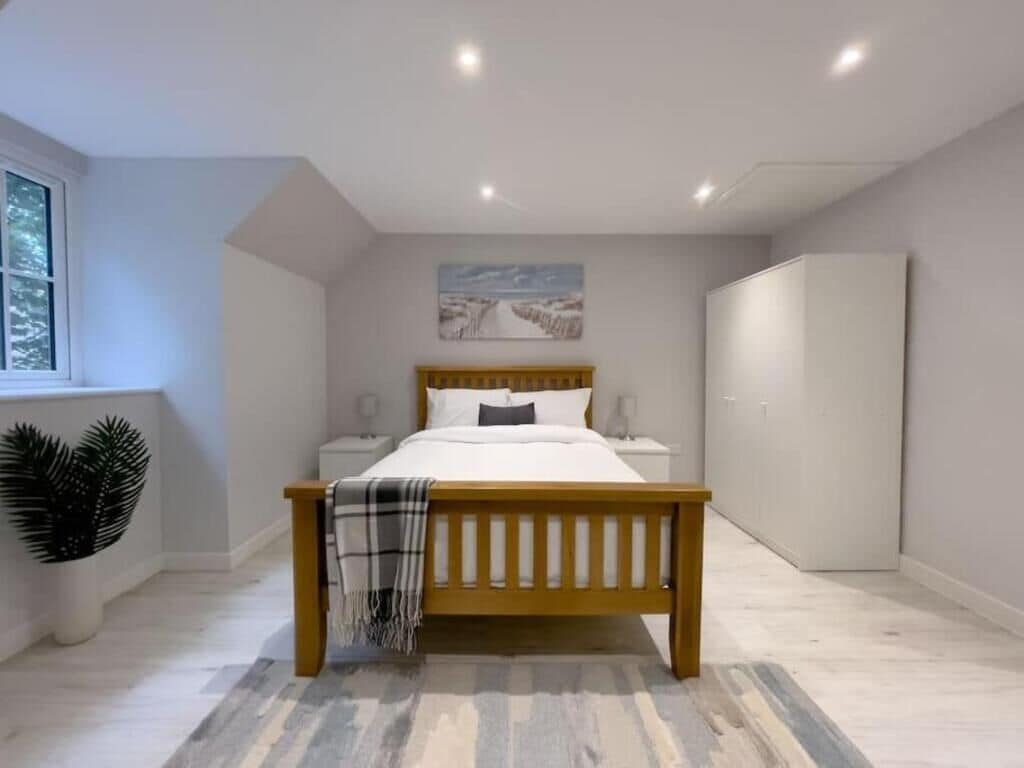 A modern bedroom with a wooden bed, a bedside table, a wardrobe, and a window with a view of trees.