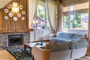 A cozy living room with a fireplace, a sofa, and a view of a house through large windows. - Spacious Apartment 4br/10p - Megeve Center (Megeve)