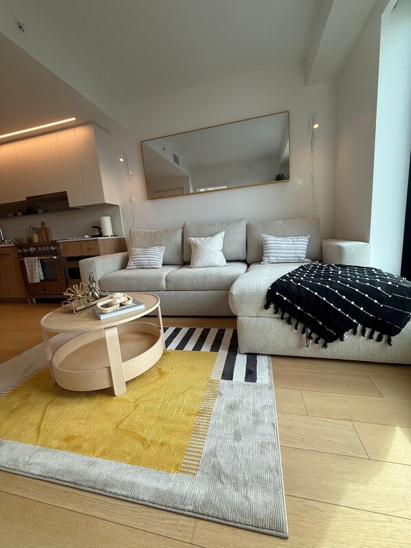Ein modernes Wohnzimmer mit Sofa, Couchtisch, Teppich und einer Küchenzeile im Hintergrund.