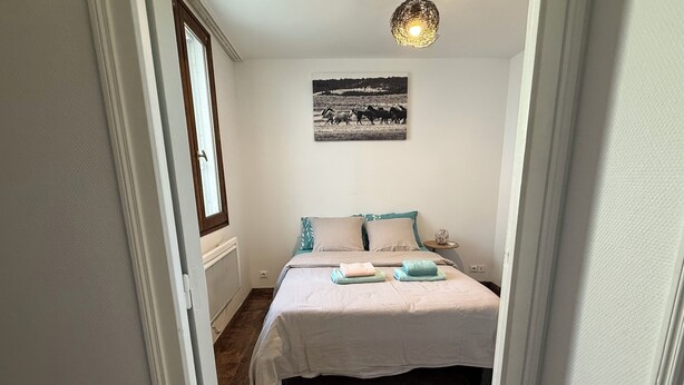 Un dormitorio con cama, mesita de noche, lámpara, ventana y un cuadro colgado en la pared.