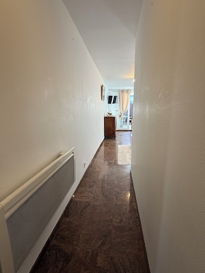 A hallway with a radiator, a wooden cabinet, and a TV on the wall. - THE CHARMING ONE-BEDROOM APARTMENT AT 15 RUE DE LA FRATERNITE (Drancy)