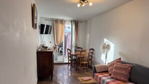 Una sala acogedora con sofá, una mesita, un ventilador, televisor y una mesa de comedor con sillas.