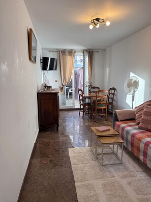 A living room with a sofa, a small table, a TV, a dining area with chairs, and a fan. - THE CHARMING ONE-BEDROOM APARTMENT AT 15 RUE DE LA FRATERNITE (Drancy)