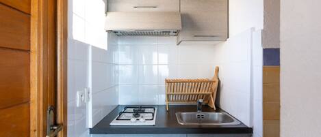 A kitchen with a gas stove, sink, and wooden drying rack.