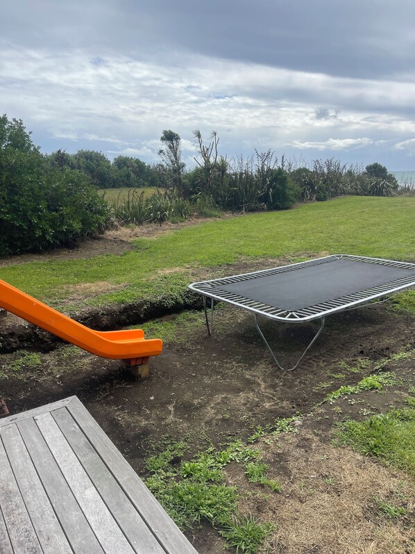 A trampoline and a slide in a grassy outdoor area. - Ocean Shores Taranaki (Warea)