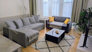 A modern living room with two grey sofas, a coffee table, and a large window with curtains. - 2 Bedroom House with Garden and Free Parking (Greater London)