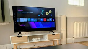 A flat-screen TV on a white stand with a shelf below, a white radiator, and a wooden table with decorative balls. - 2 Bedroom House with Garden and Free Parking (Greater London)