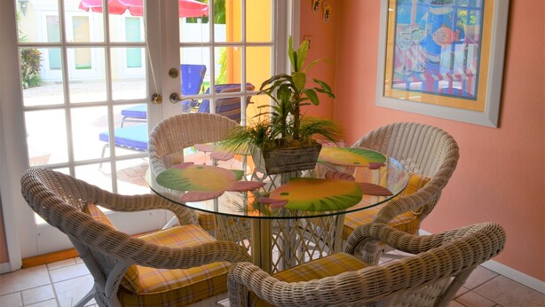 A dining area with wicker chairs, a glass table, and a potted plant. - Charming one floor, 2-bedroom house steps to the beach, private heated pool (Holmes Beach)