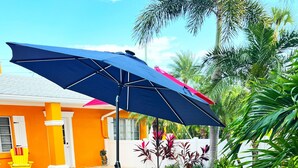A patio area with a round table and benches, surrounded by tropical plants and a pool. - Charming one floor, 2-bedroom house steps to the beach, private heated pool (Holmes Beach)