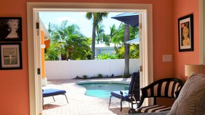 A bedroom with a view of a swimming pool, a chair, and a bed with a pillow. - Charming one floor, 2-bedroom house steps to the beach, private heated pool (Holmes Beach)