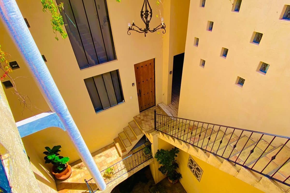 Une cour intérieure à plusieurs niveaux, avec un escalier, des plantes en pot et une plante suspendue.