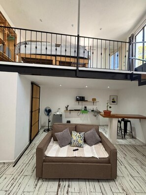 Un moderno spazio abitativo in stile loft con soffitto alto, un divano, un'area pranzo e una cucina.