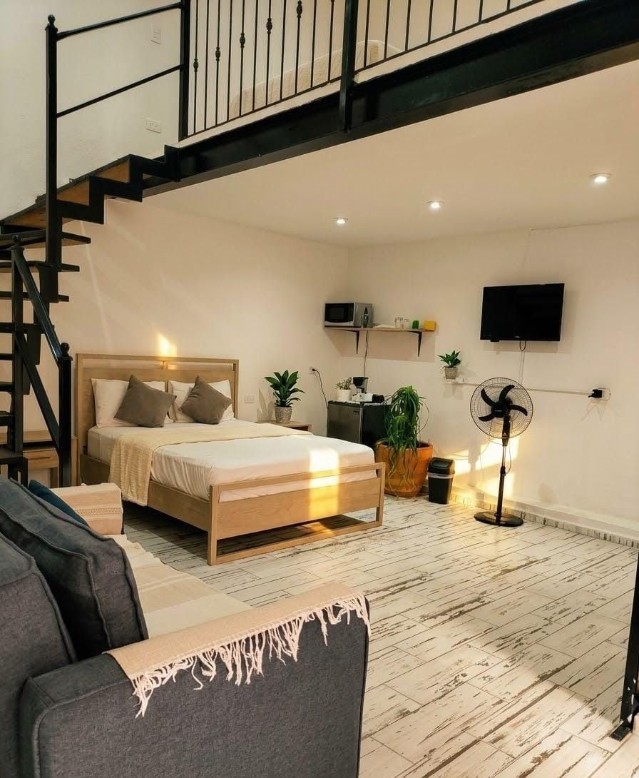 A bedroom with a bed, a desk, a chair, a TV, a fan, and a staircase.
