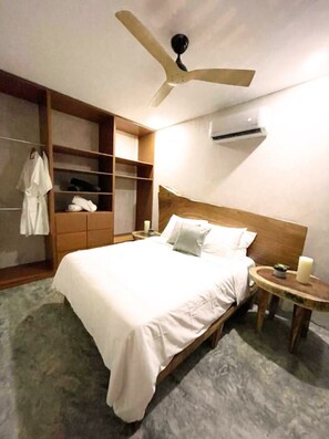 A bedroom with a bed, a wooden wardrobe, a ceiling fan, an air conditioning unit, and a bedside table with a candle. - Depa 2 rec y alberca privada en veleta Tulum (Tulum)