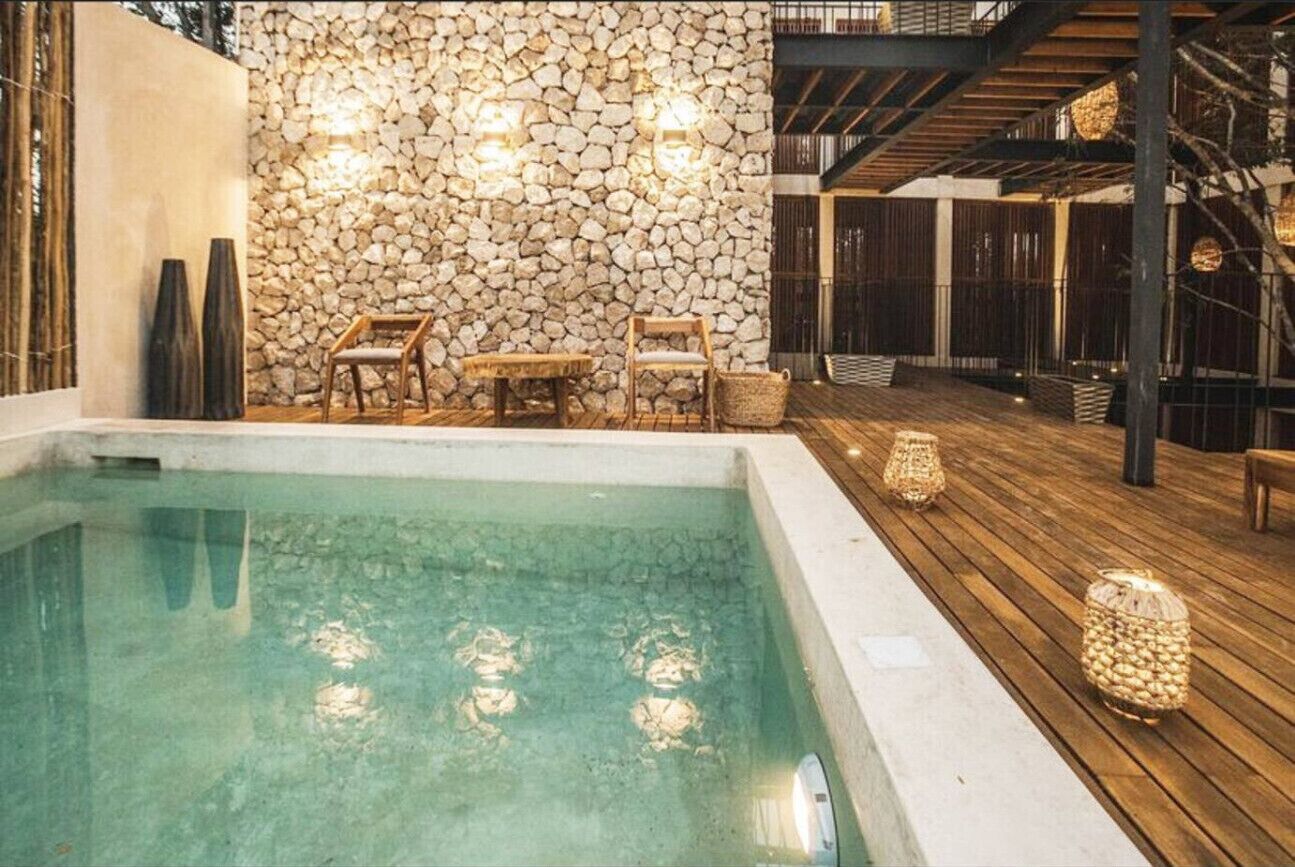 Uma área de piscina com paredes de pedra, deck de madeira e mobiliário externo.