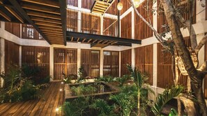 Un ampio giardino interno con passerelle in legno, barriere in bambù e vegetazione rigogliosa.