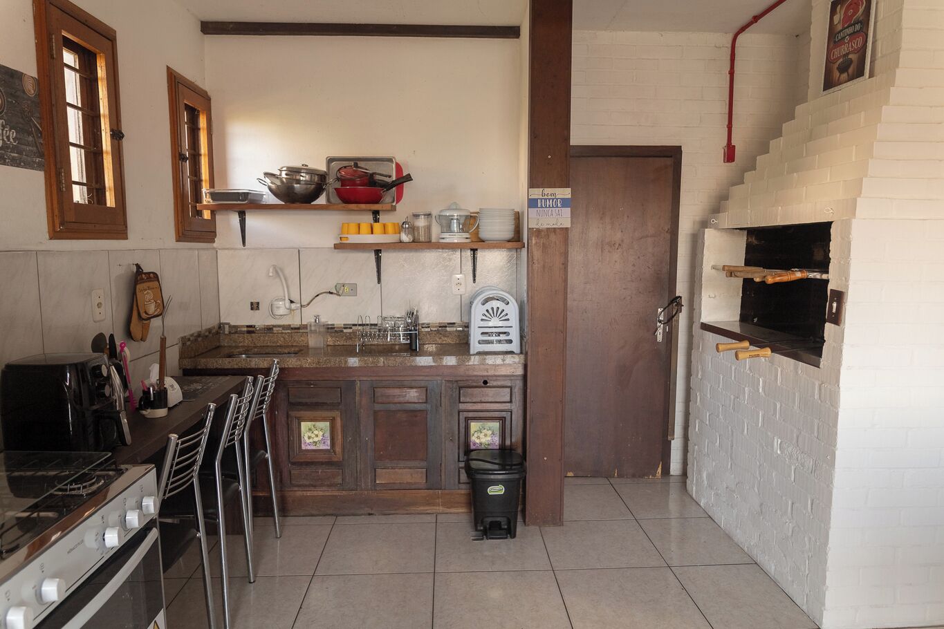 Een keuken met een fornuis, spoelbak en een pizzaoven. Er zijn kastjes, een plank met keukengerei en een afvalbak.
