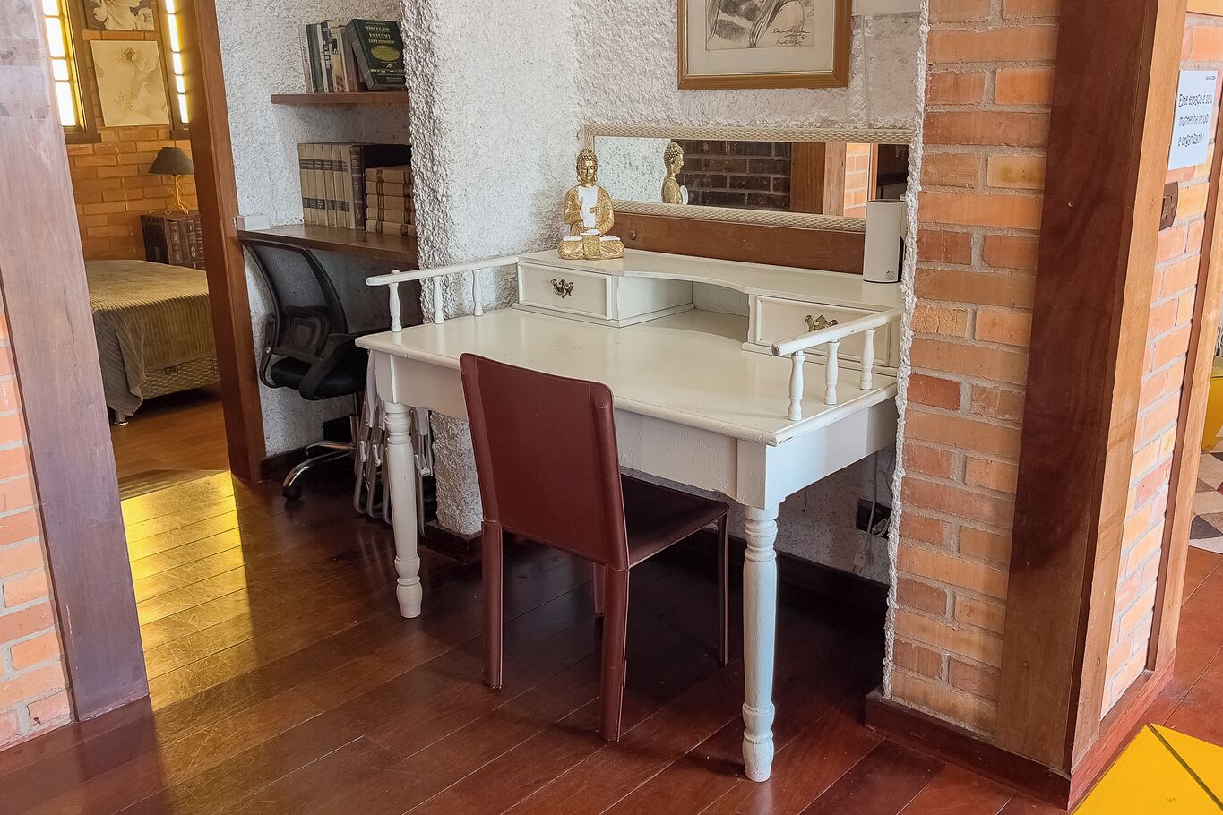 Een klein wit bureau met een stoel, een beeldje en boeken op een plank.