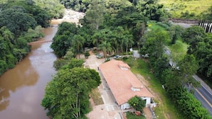 An aerial view of a rural area with a river, a bridge, and a building with a red roof. - Pousada Karandá (Serra Negra)