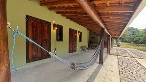 A hammock under a wooden pergola, a green wall, and a brick pathway leading to a bench. - Pousada Karandá (Serra Negra)