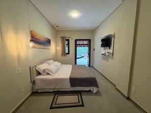 A bedroom with a bed, a painting, a TV, and a view through the door. - Pousada Karandá (Serra Negra)