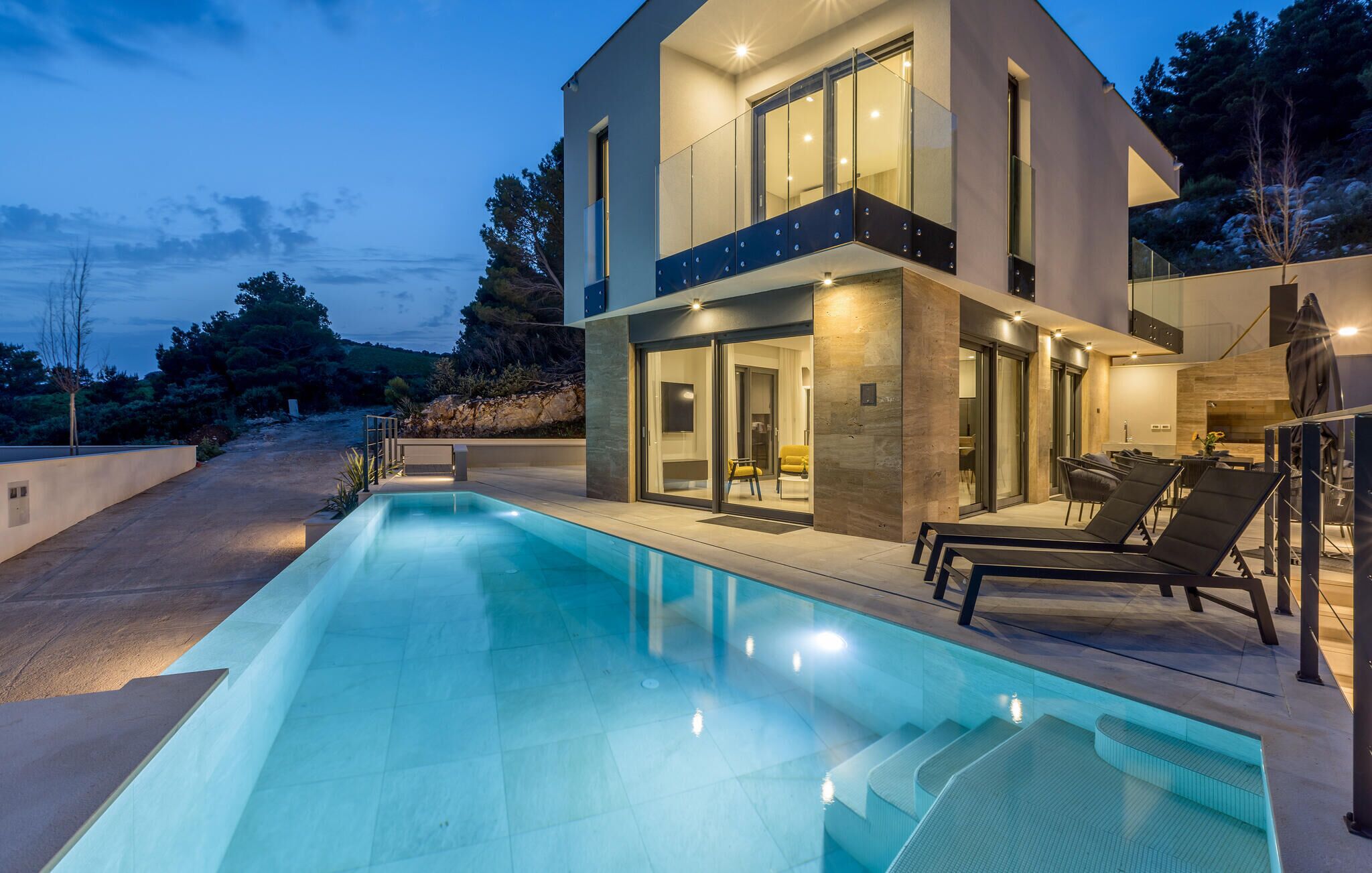 Une maison moderne à deux étages, dotée d’une piscine, d’un espace salon extérieur et d’un balcon bien éclairé.