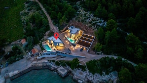 Eine Vogelperspektive eines modernen, zweistöckigen Hauses mit Schwimmbad, gelegen in der Nähe eines Gewässers, umgeben von viel Grün.