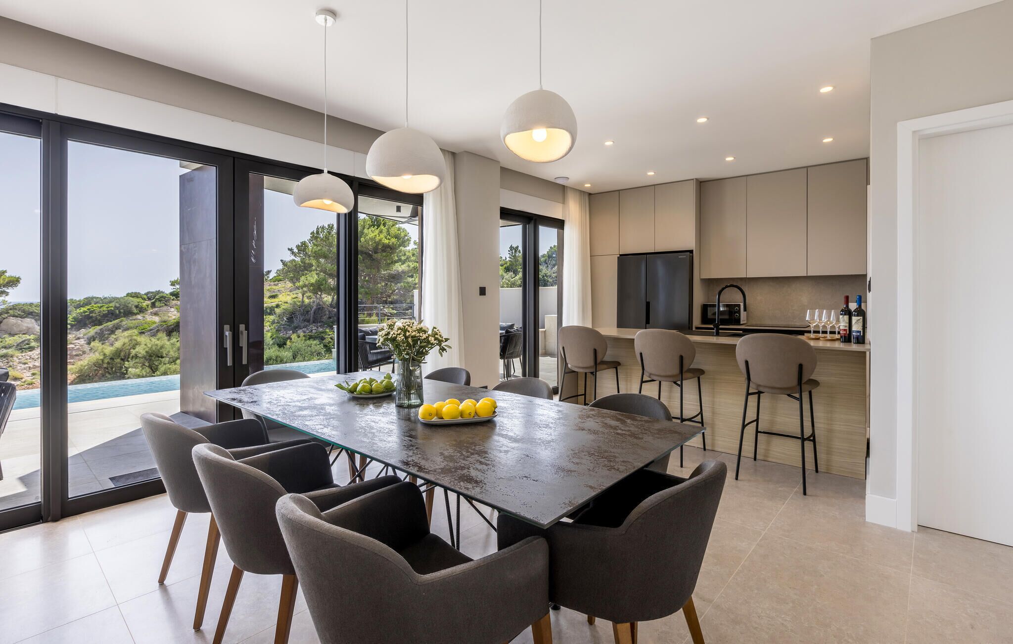 A modern kitchen with a large island, a dining area with a glass table, and a view of the outdoors.