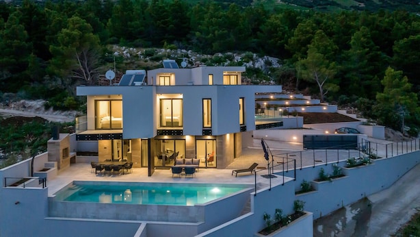 Ein modernes, zweistöckiges Haus mit Swimmingpool, Sitzgelegenheiten im Freien und Solaranlage.