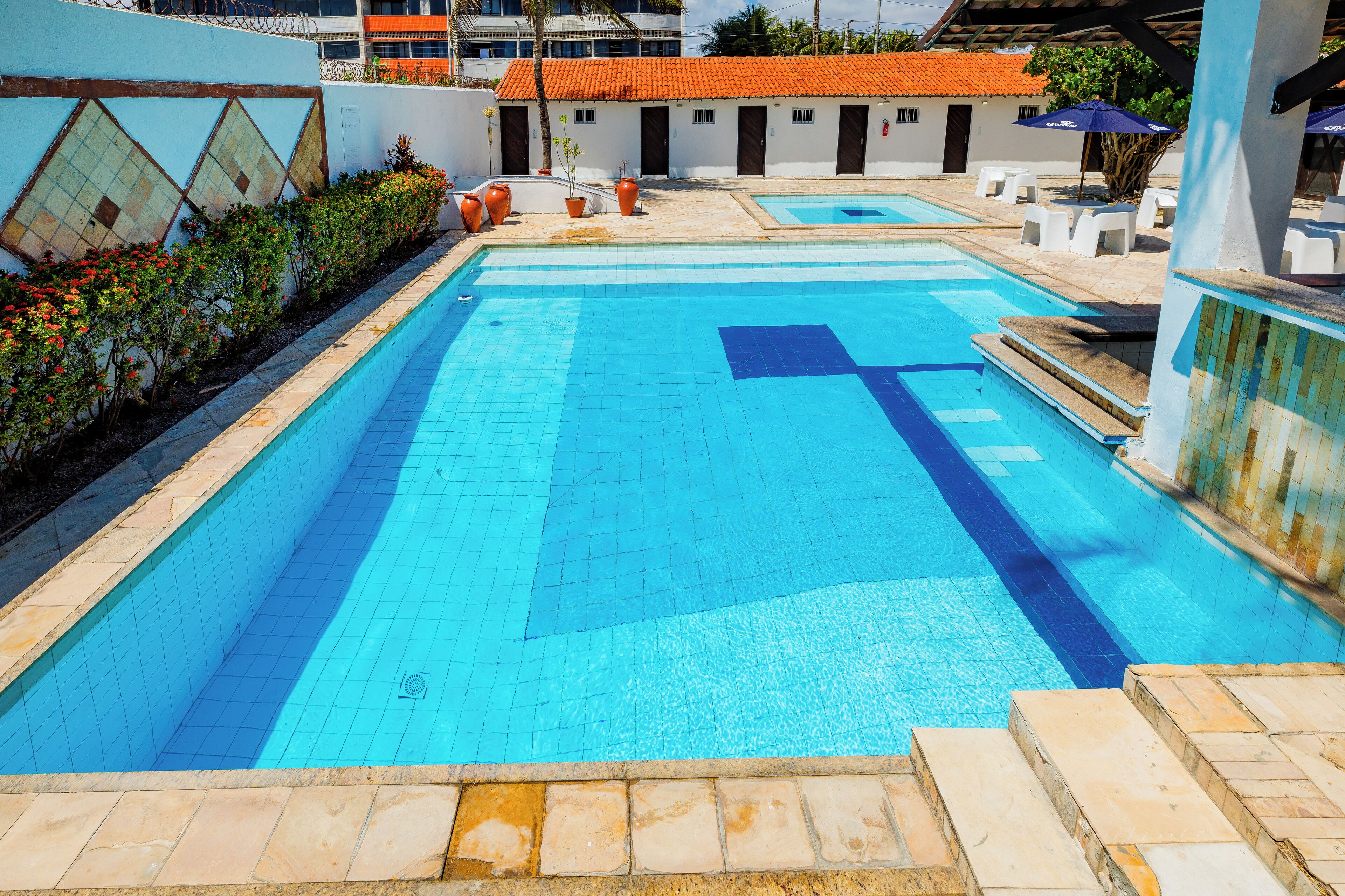 A rectangular swimming pool with a tiled deck, surrounded by a low wall with a geometric pattern.
