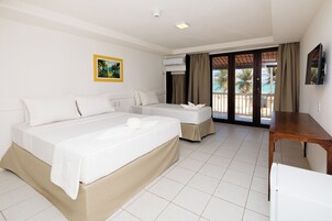 Quarto de hotel com duas camas, uma mesa de madeira, televisão e varanda com vista para palmeiras.