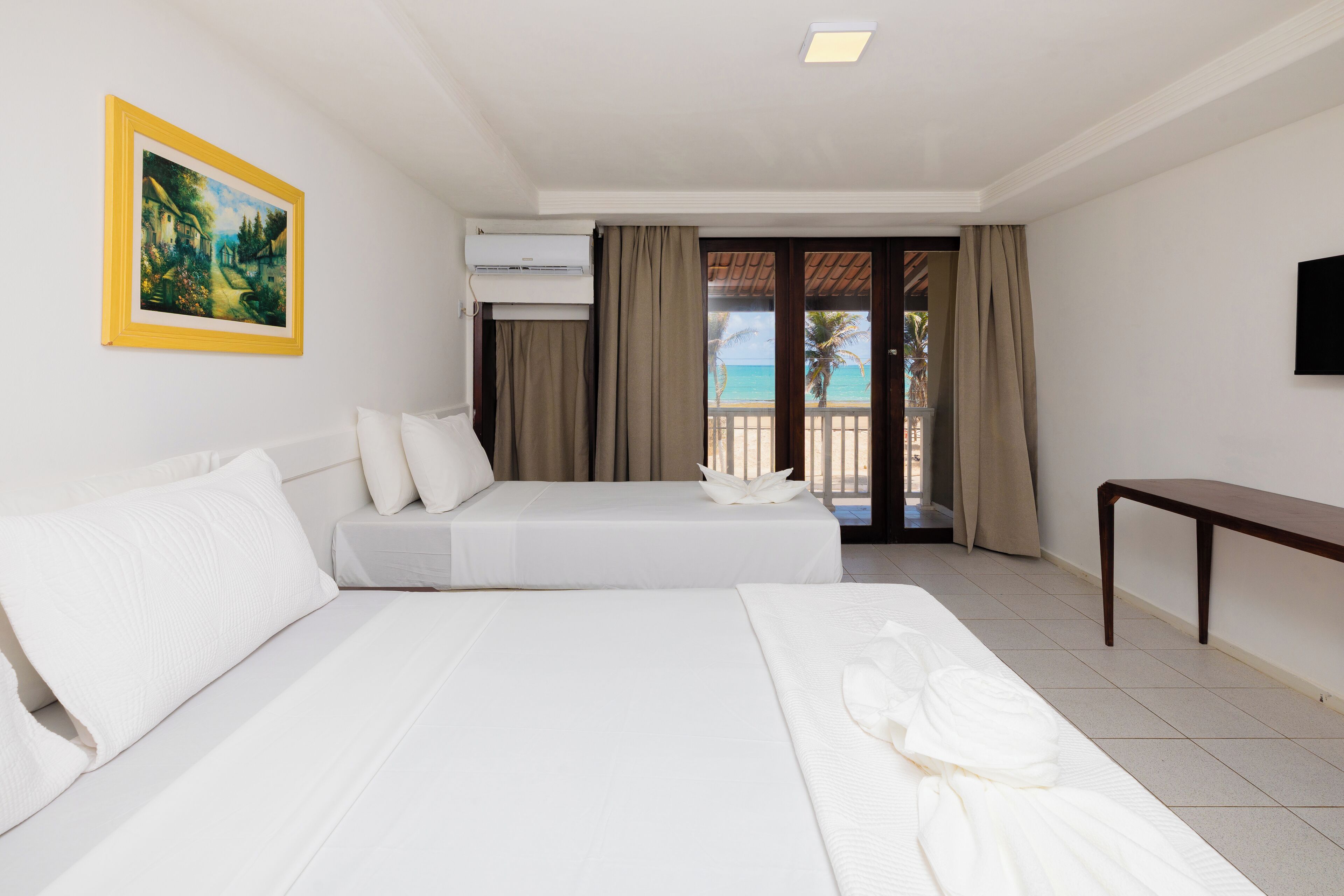 Habitación de hotel con dos camas, un televisor de pantalla plana, un cuadro y un balcón con vista al mar.