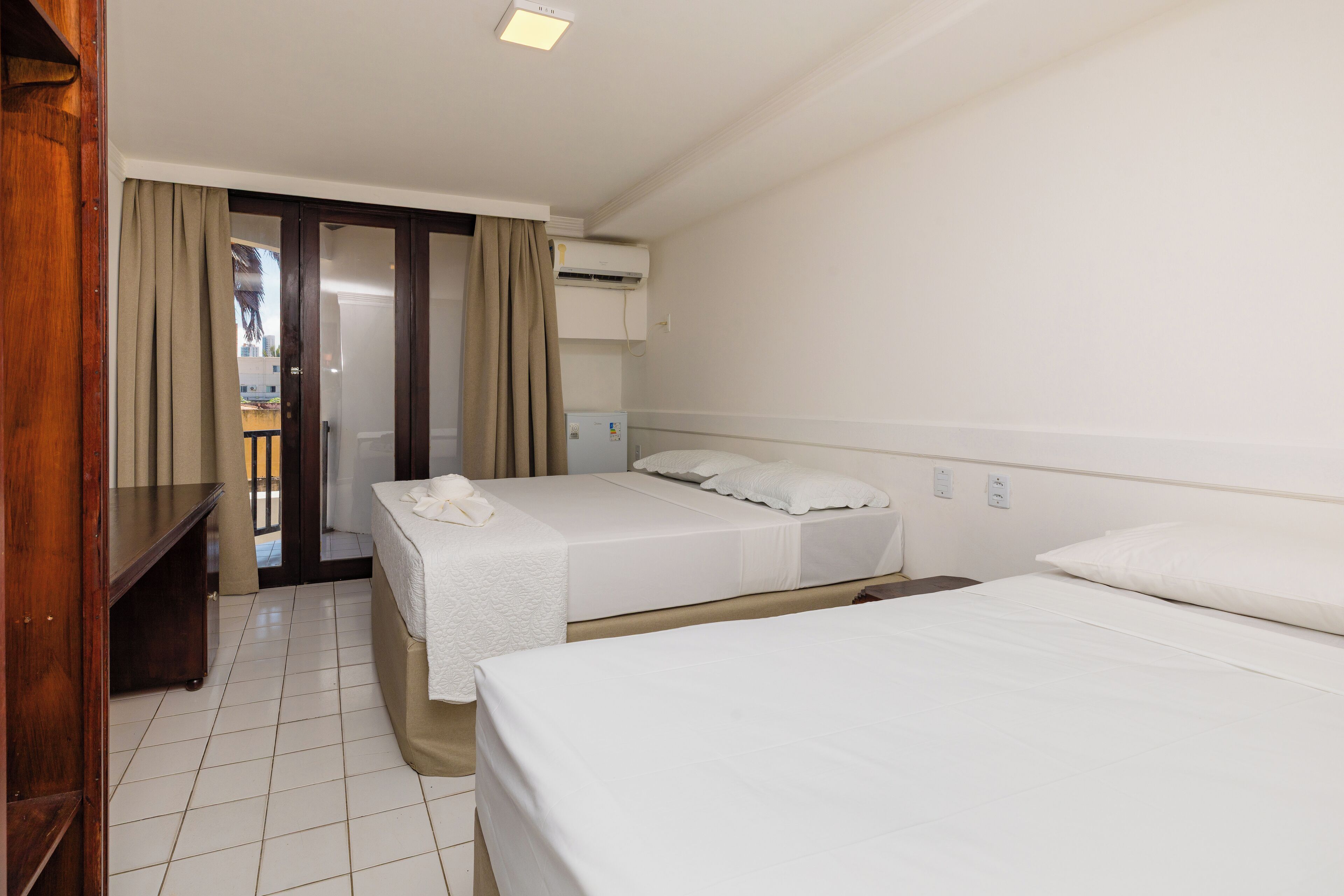 Habitación de hotel con dos camas individuales, una mesita de noche de madera, un armario y un armario corredero que da a un balcón.