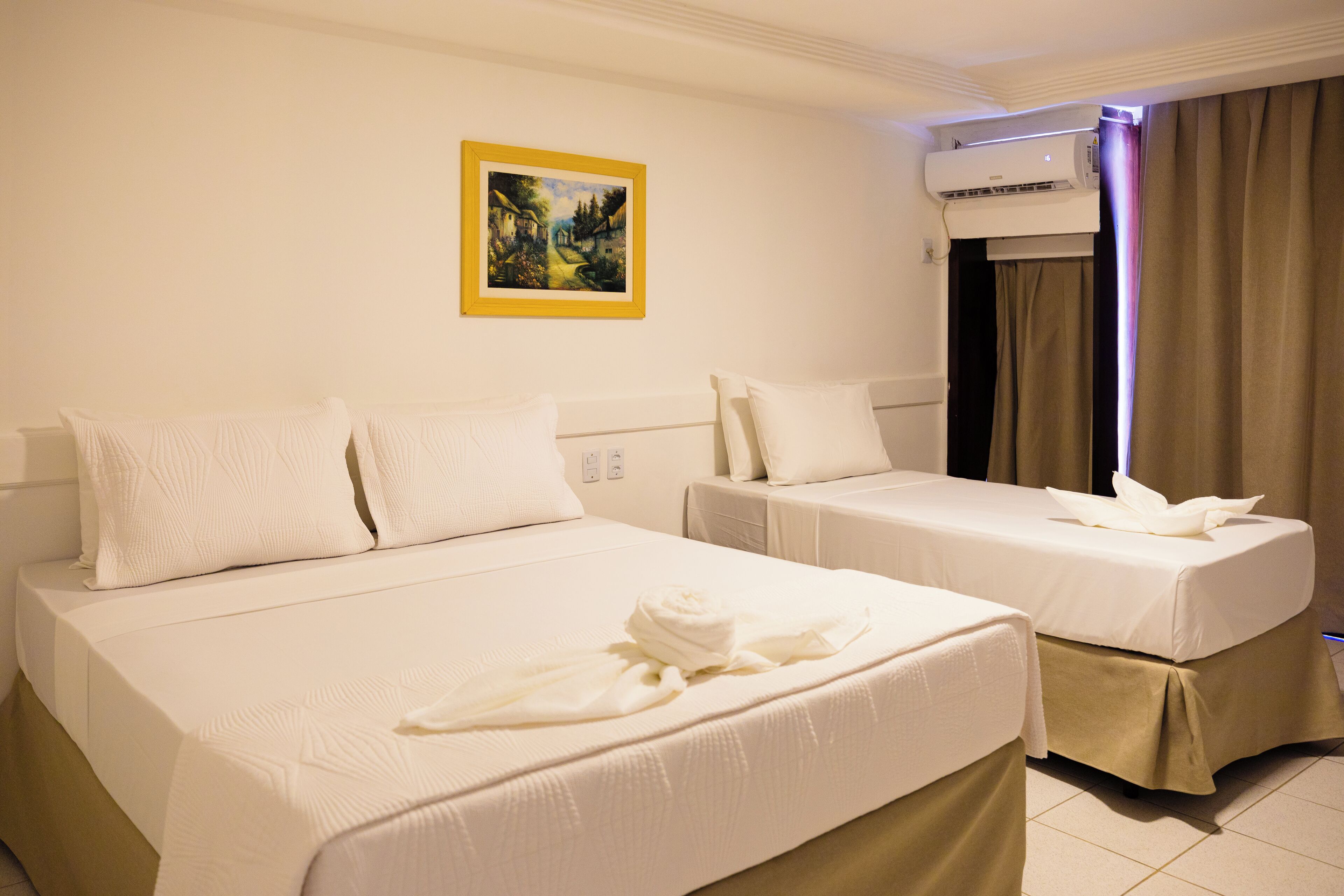 A hotel room with two beds, a painting on the wall, an air conditioning unit, and a curtain.