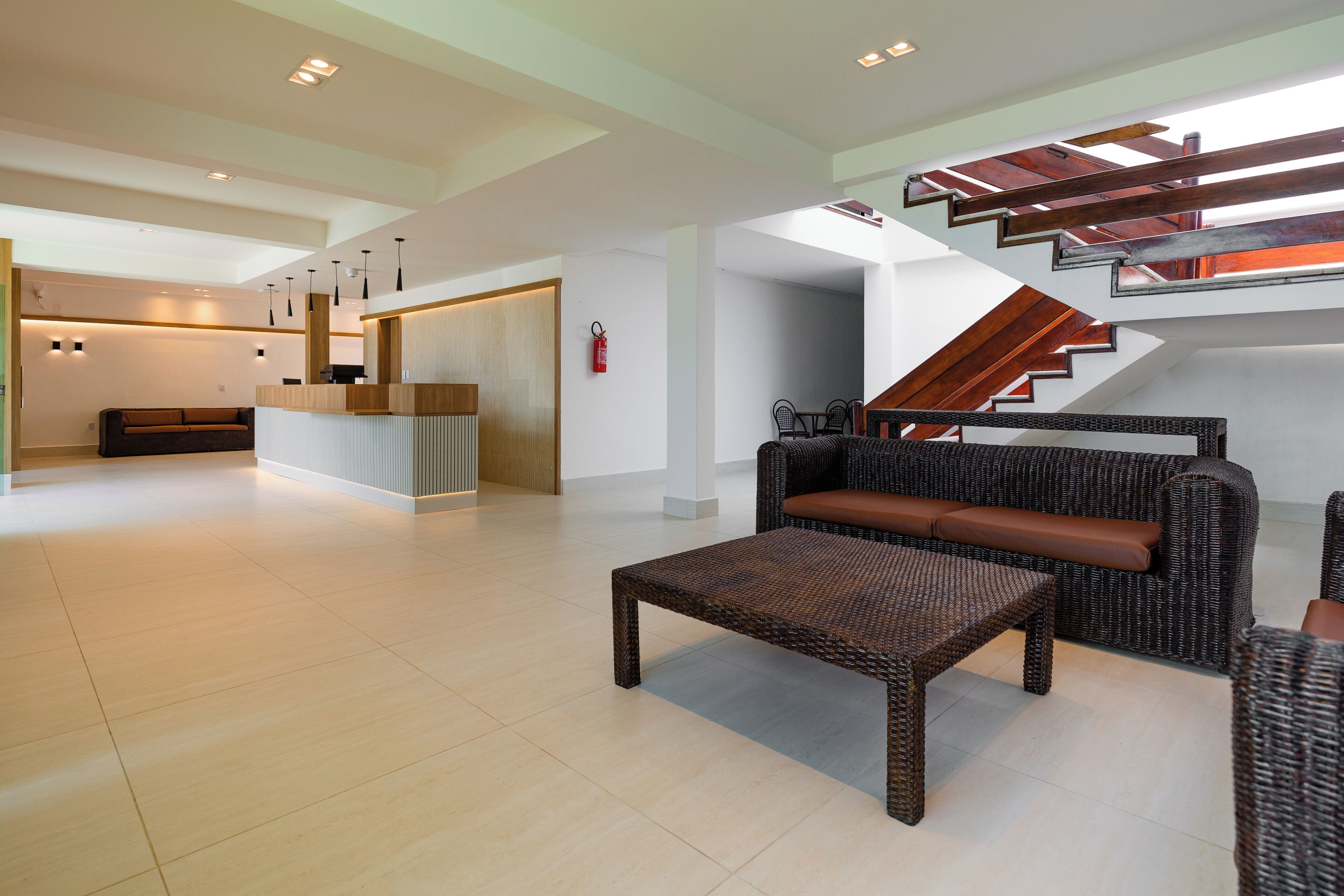 Un vestíbulo amplio con una mesa de recepción, una escalera de madera y un área de descanso con un sofá y un banco de mimbre.