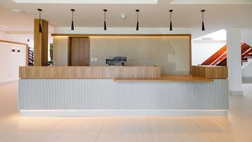 Bancada de recepção com acabamento em madeira, base branca e luminárias pendentes pretas.