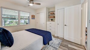 Ein Schlafzimmer mit Bett, Deckenventilator, Fenster und Einbauschränken.
