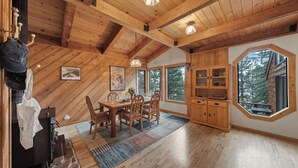 A wooden interior with a dining area, a kitchen with wooden cabinets, and large windows offering a view of trees. - Cozy Donner Lake Cabin w/ Kayaks, Forest Views, Fireplace & Quick Ski Resort Access Donner Lake Refuge by Avantstay (Truckee)