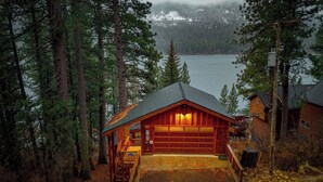 A cabin with a wooden exterior, a garage, and a view of a lake surrounded by trees. - Cozy Donner Lake Cabin w/ Kayaks, Forest Views, Fireplace & Quick Ski Resort Access Donner Lake Refuge by Avantstay (Truckee)