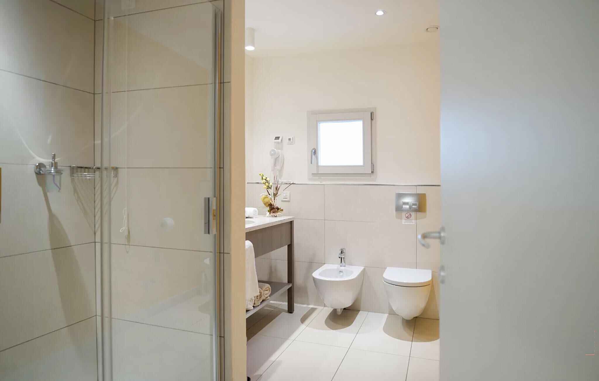 Un baño moderno con cabina de ducha de vidrio, un bidé, un inodoro y un tocador con espejo.