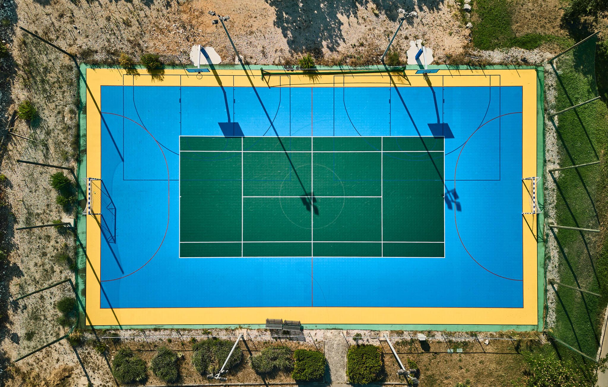 An aerial view of a tennis court with surrounding greenery and fencing.