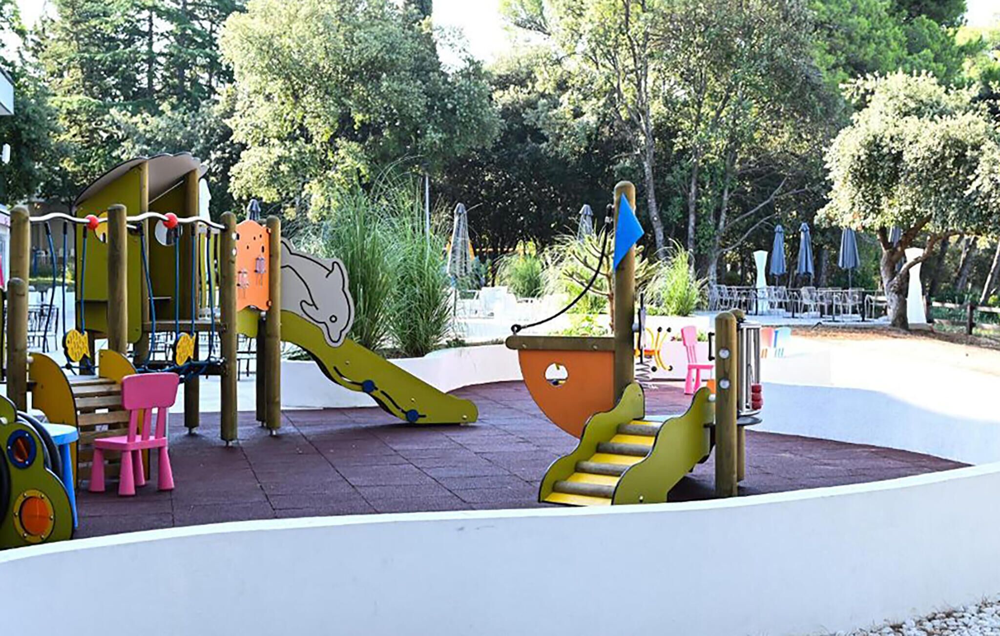 A playground with slides and climbing structures, surrounded by trees and outdoor seating.