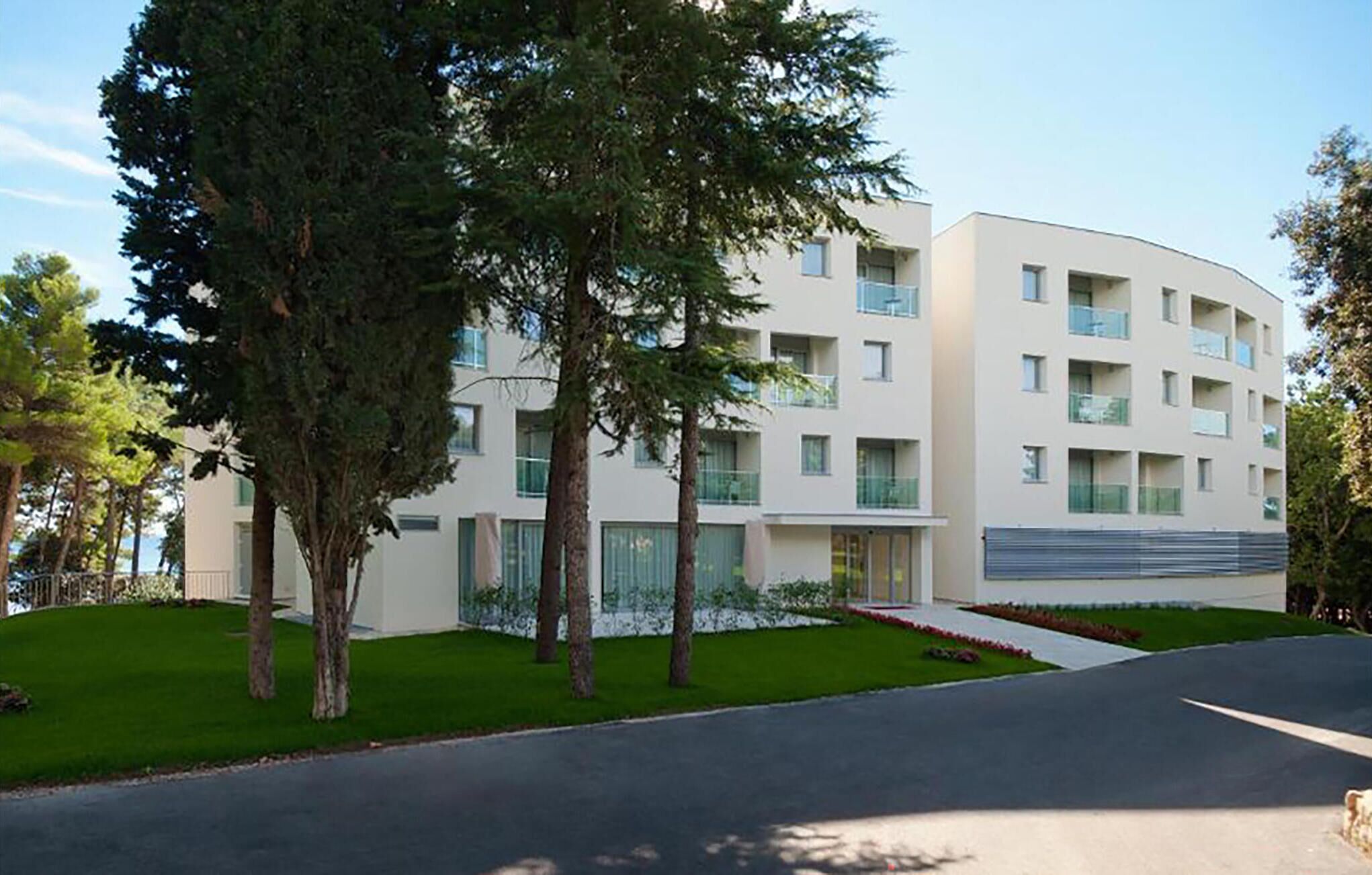 A modern multi-story building with a curved facade, large windows, and a well-maintained lawn.