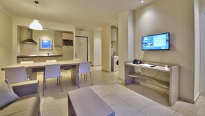 Ein modernes Hotelzimmer mit Essbereich, einer Küche, einem Fernseher und einem Schreibtisch mit Telefon.