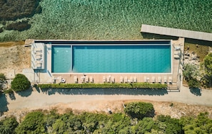 Eine Vogelperspektive auf einen rechteckigen Pool mit Holzterrasse und Liegestühlen.