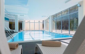 A modern indoor swimming pool with clear glass walls, lounge chairs with towels, and a view of the outdoors. - Lovely apartment in Biograd with sauna (Biograd)