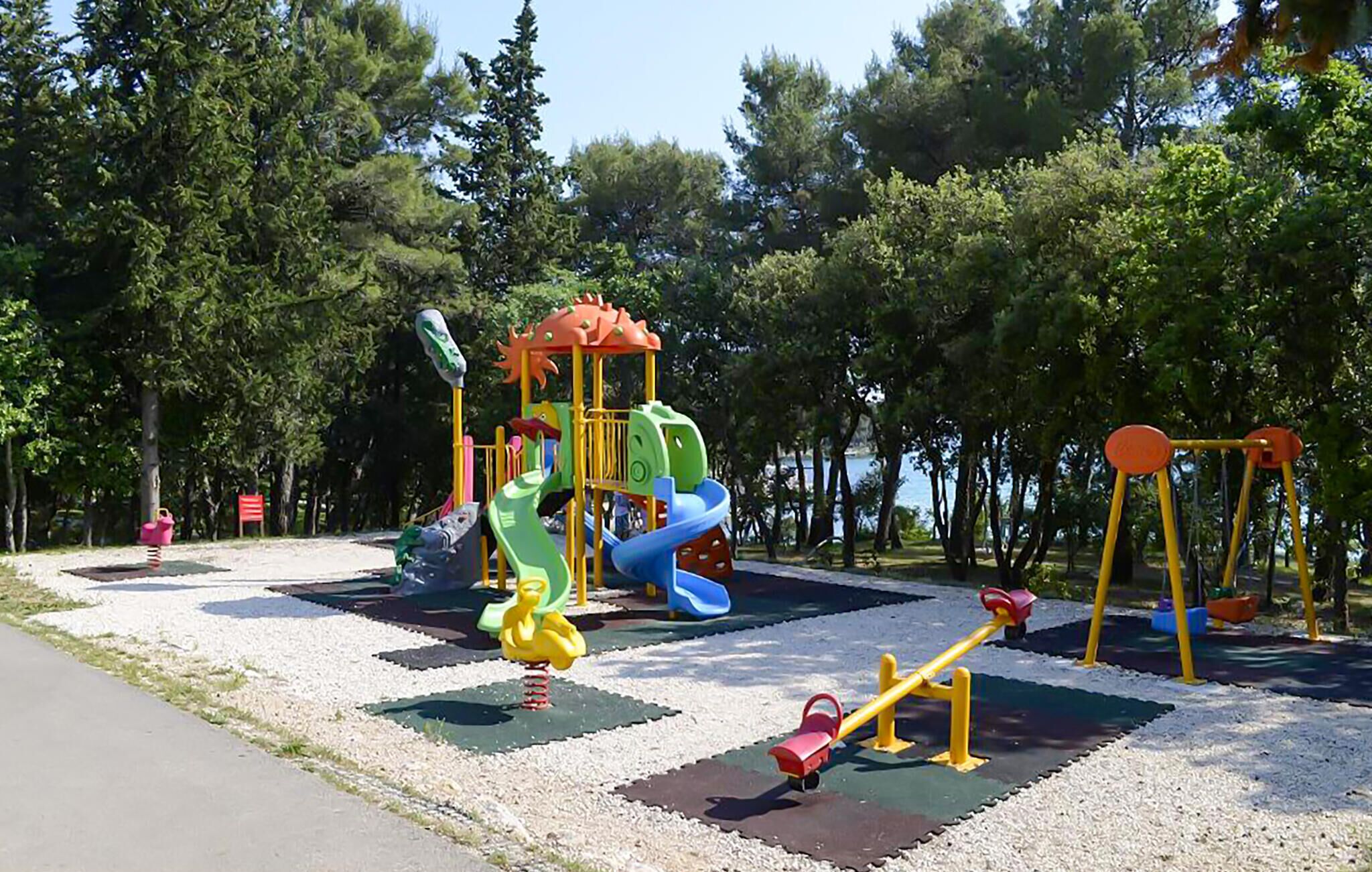 A playground with various play structures including slides and swings, surrounded by trees.