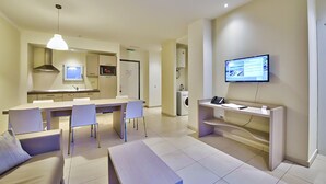 Uma sala de estar moderna com área de jantar, cozinha e televisão na parede.